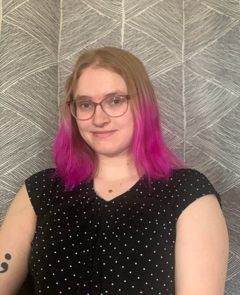 Jazmyne looking ahead with a slight smile. She's wearing glasses and a black shirt with white dots.